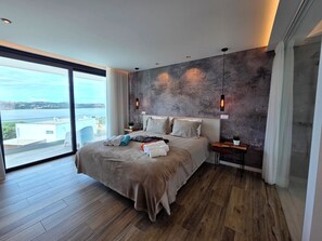 Ein modernes Schlafzimmer mit einem großen Bett, Meerblick und einer Wand mit Betonoptik.