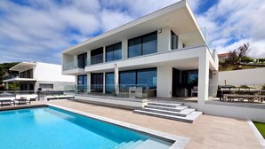 Una casa moderna de dos plantas con piscina, ventanas grandes y techo plano.