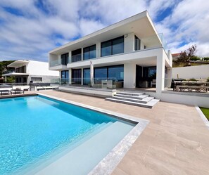 Ein modernes, zweistöckiges Haus mit Swimmingpool, großen Fenstern und einer Flachdach.