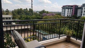 Ein Balkon mit einem Stuhl, Blumentöpfen und Blick auf ein Gebäude und Grünflächen.
