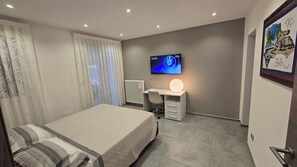 Une chambre à coucher avec un lit, un bureau, un écran d’ordinateur et un radiateur.
