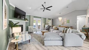 A modern living room with a fireplace, a ceiling fan, and a television mounted on the wall.