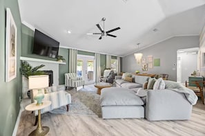 A modern living room with a fireplace, a ceiling fan, and a television mounted on the wall.