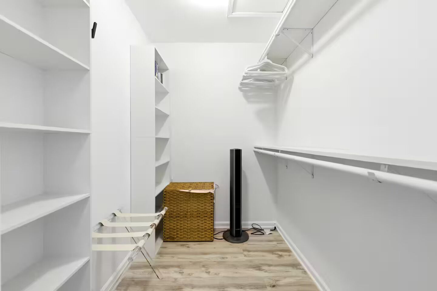 A narrow hallway with white walls, wooden flooring, and built-in shelving units.