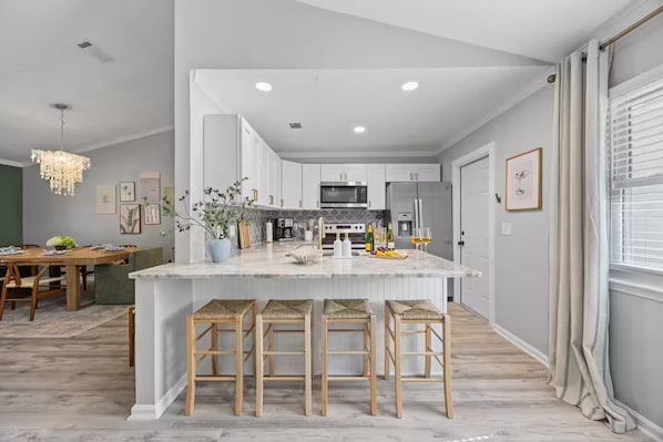 A modern kitchen with white cabinets, a marble island, and bar stools.