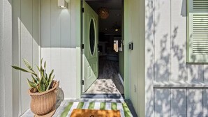 A house entrance with a green door, a potted plant, and a striped mat.