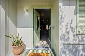A house entrance with a green door, a potted plant, and a striped mat.