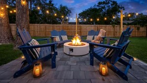 An outdoor seating area with a circular fire pit, surrounded by lounge chairs and string lights.