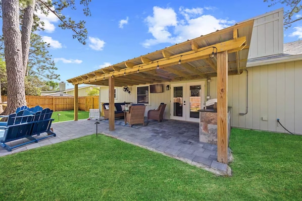 A covered patio with outdoor furniture, a grill, and a wooden pergola.