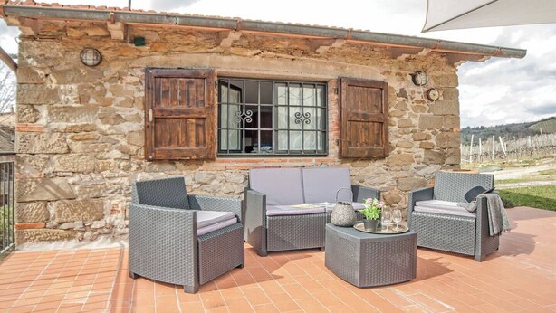 A stone building with a tiled patio, wicker furniture, and a window with shutters. - COUNTRY HOUSE (Greve in chianti)
