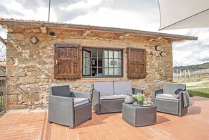 Ein Steinhaus mit einer gefliesten Terrasse, Korbmöbeln und einem Fenster mit Fensterläden.