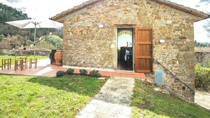 A stone building with a wooden door, a patio with chairs and a table, and a view of the surrounding landscape. - COUNTRY HOUSE (Greve in chianti)