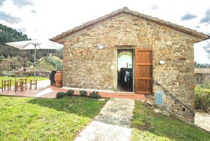 A stone building with a wooden door, a patio with chairs and a table, and a view of the surrounding landscape. - COUNTRY HOUSE (Greve in chianti)