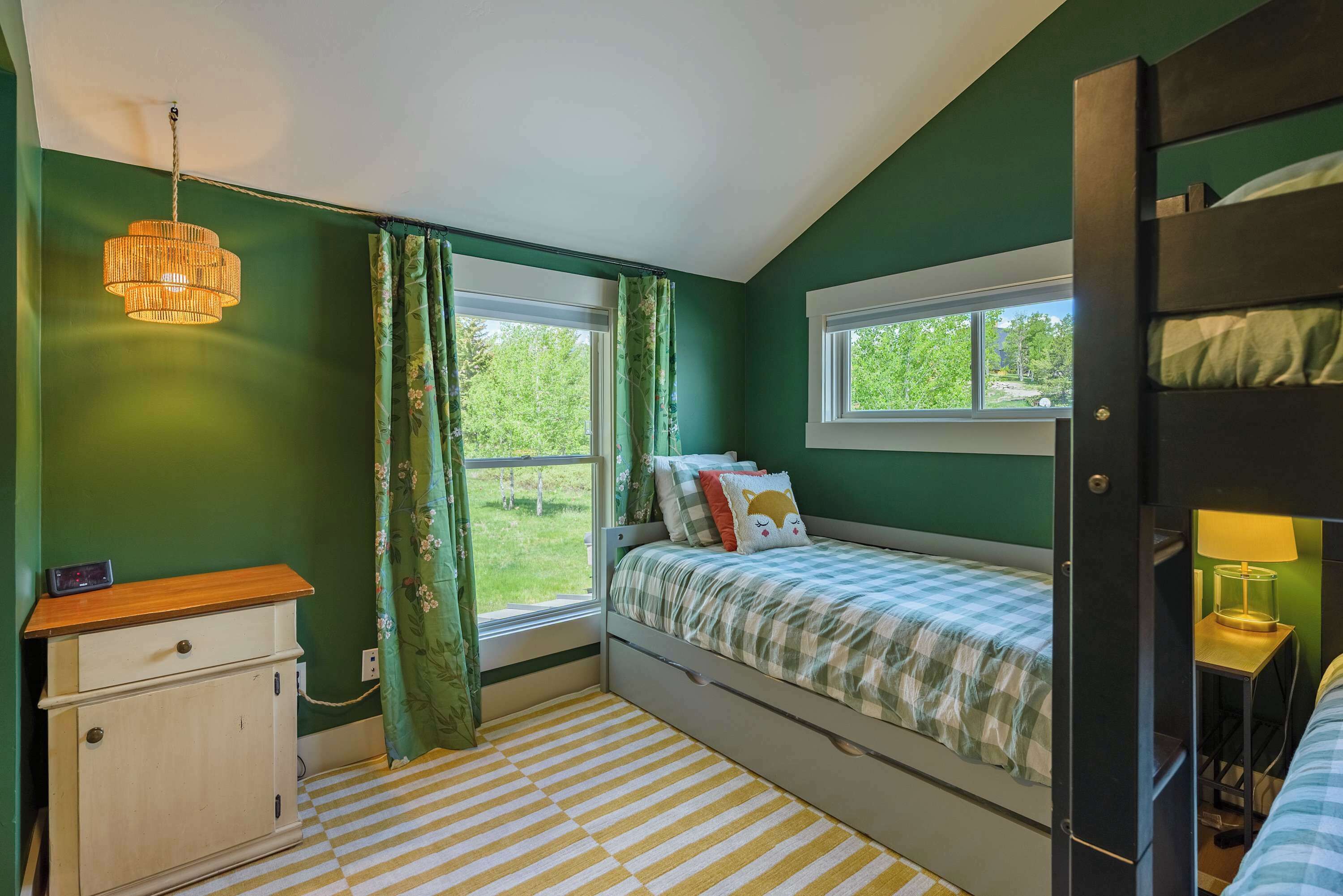 A room with a bunk bed, a desk, a chair, a lamp, and a window with curtains.