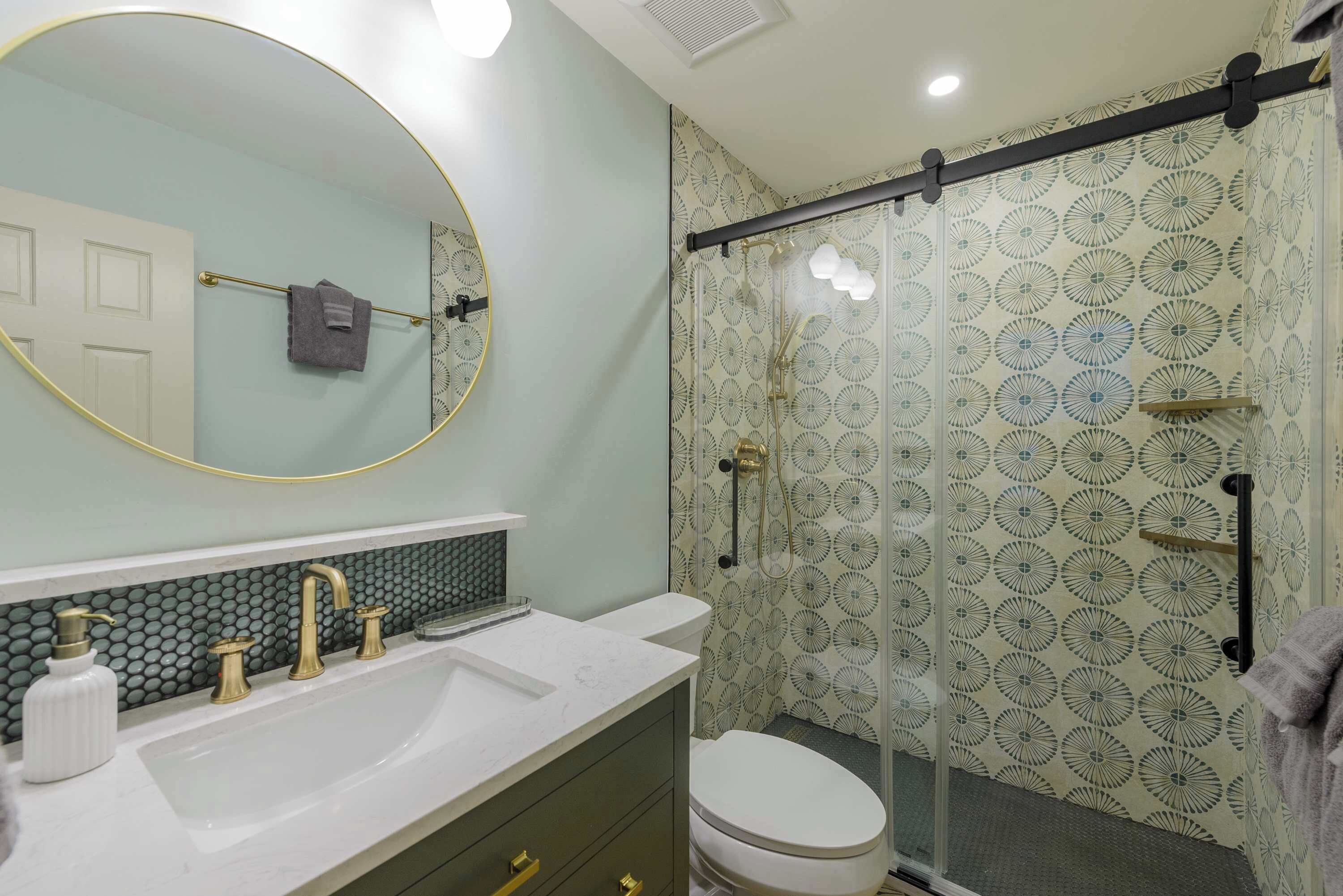 A bathroom with a white sink, gold faucets, a mirror, and a shower with patterned glass doors.