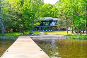 Ein modernes Haus mit einer Holzsteg, der zu einem Teich führt, umgeben von Bäumen.