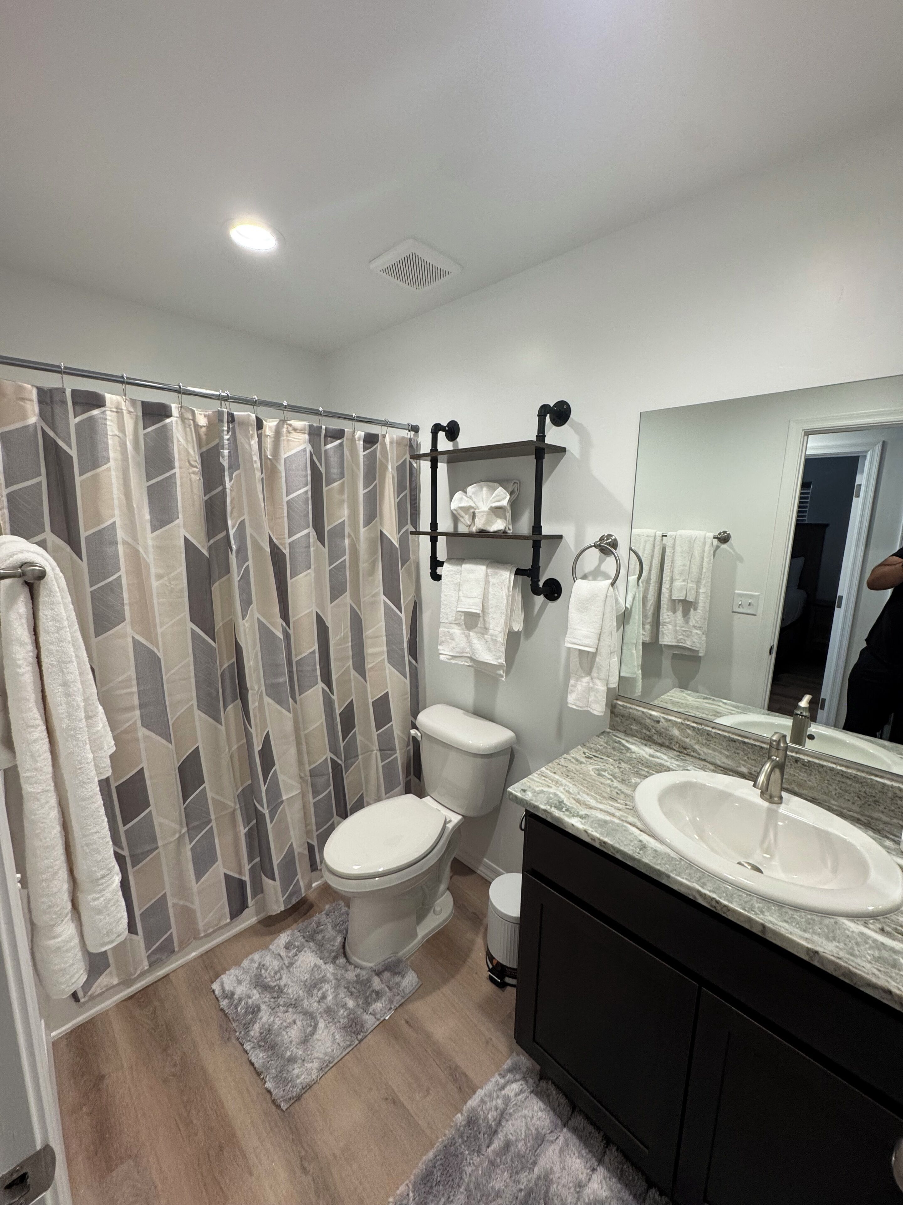 A bathroom with a shower curtain, toilet, sink, and mirror.