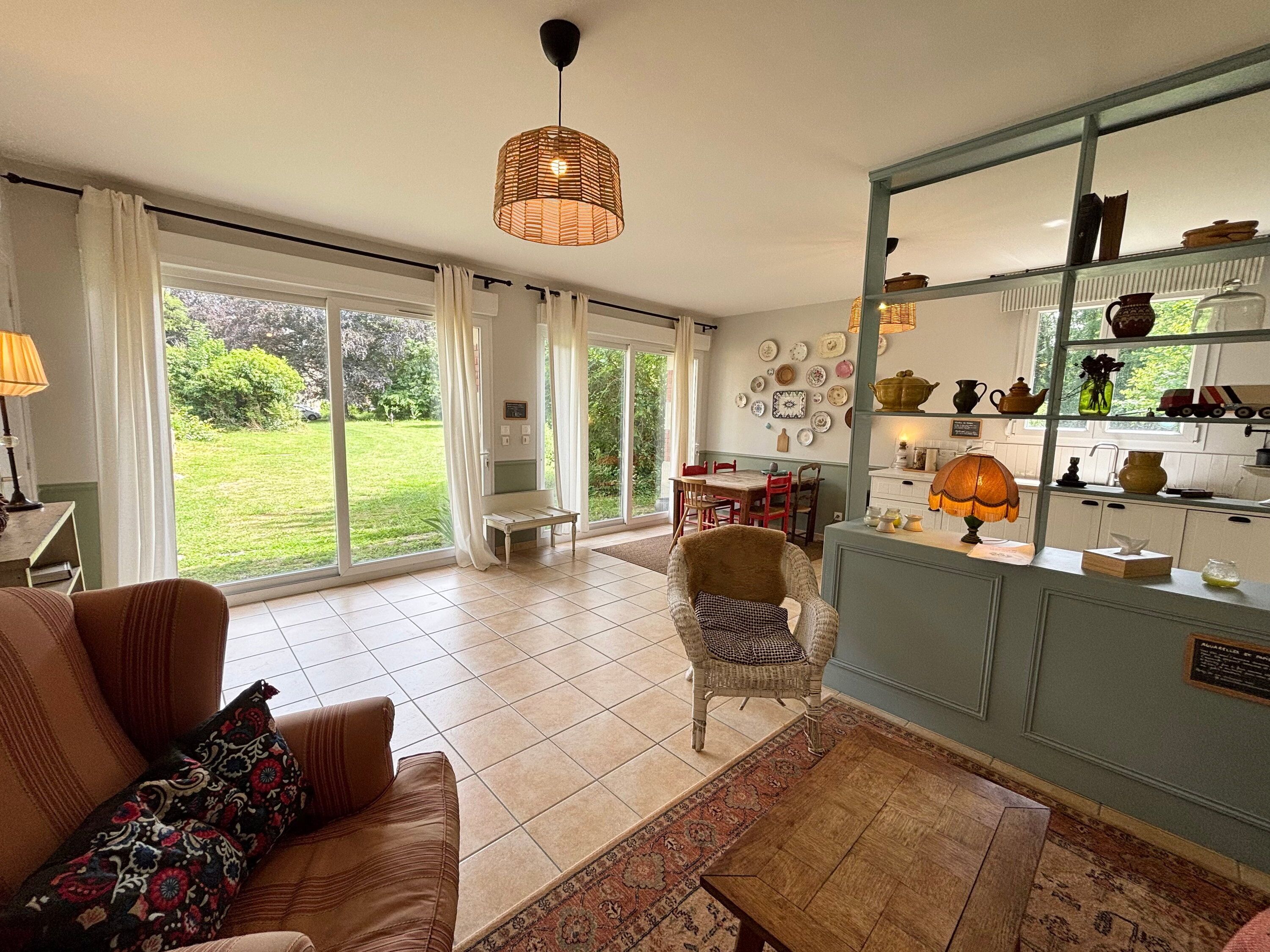 A living room with a sofa, a chair, a dining table, and a kitchen area with shelves. - Petite maison à l'orée du bois (Sillery)