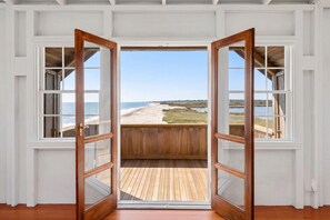 Une porte en bois ouverte donnant sur un balcon d’où l’on peut admirer une plage et l’océan.