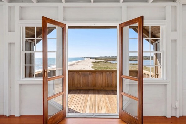 Una puerta de madera abierta que da a un balcón con vista a una playa y al océano.