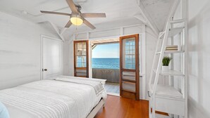 A bedroom with a bed, a ceiling fan, a wooden floor, and a view of the sea through open doors. - Oceana: Beachfront Estate, Period Charm, Sleeps 8 (South Kingstown)