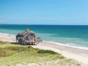 Una casa frente a la playa con balcón, chimenea y vista al océano.