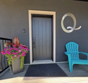 A door with a keypad lock, a large planter with pink flowers, and a blue chair on the porch.