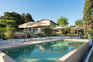 A swimming pool with lounge chairs and umbrellas, surrounded by greenery and a building. - Il Poggione 10, Emma Villas (Crocino)