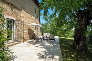 An outdoor patio with stone flooring, a table with chairs, and a large umbrella. - Il Poggione 10, Emma Villas (Crocino)