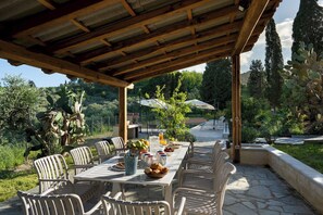 An outdoor covered patio with a table set for dining, surrounded by chairs, and a view of a garden with cacti and trees. - Il Poggione 10, Emma Villas (Crocino)
