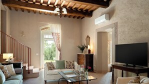 Ein Wohnzimmer mit Sofa, Sesseln, Couchtisch, Fernseher, Kamin und einer Treppe zu einem Balkon.