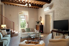 A living room with a sofa, armchairs, a coffee table, a TV, a fireplace, and a staircase leading to a balcony. - Il Poggione 10, Emma Villas (Crocino)