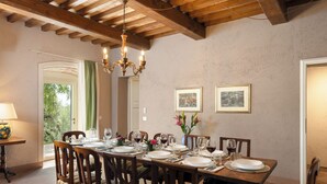 Ein Esszimmer mit einem Holztisch, gedeckt für sechs Personen, umgeben von Stühlen, einer Kristallleuchtre und gerahmten Kunstwerken an den Wänden.