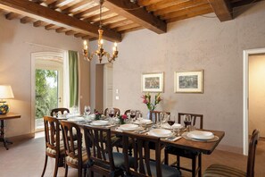 A dining room with a wooden table set for six, surrounded by chairs, a chandelier, and framed artwork on the walls. - Il Poggione 10, Emma Villas (Crocino)