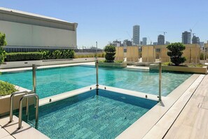 Ein Dachpool mit klarem, blauem Wasser, umgeben von einer gefliesten Terrasse und einer niedrigen Mauer mit Grünpflanzen.