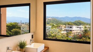 Ein Badezimmer mit zwei Waschbecken, einem Spiegel und einem Fenster mit Blick auf eine Stadtlandschaft und Berge.