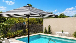 Ein Schwimmbecken mit Liegestühlen und einem gestreiften Sonnenschirm.