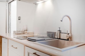 Uma cozinha moderna com bancada branca, pia de aço inoxidável e escorredor de louça.