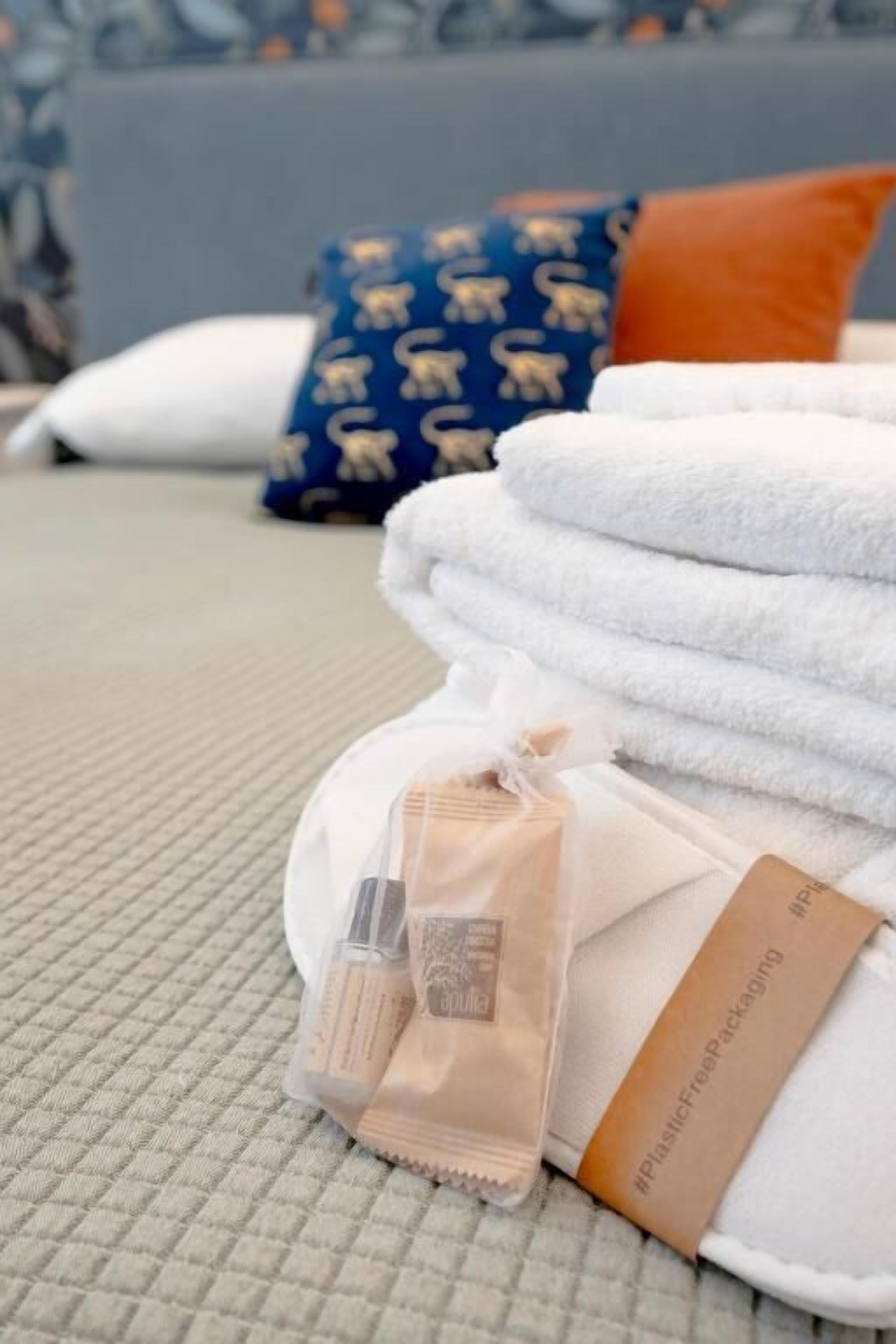 Un lit avec des serviettes blanches soigneusement pliées, un oreiller beige et un oreiller bleu à motifs.