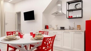 Una cucina moderna con mobili bianchi, una televisione a schermo piatto e sedie rosse.
