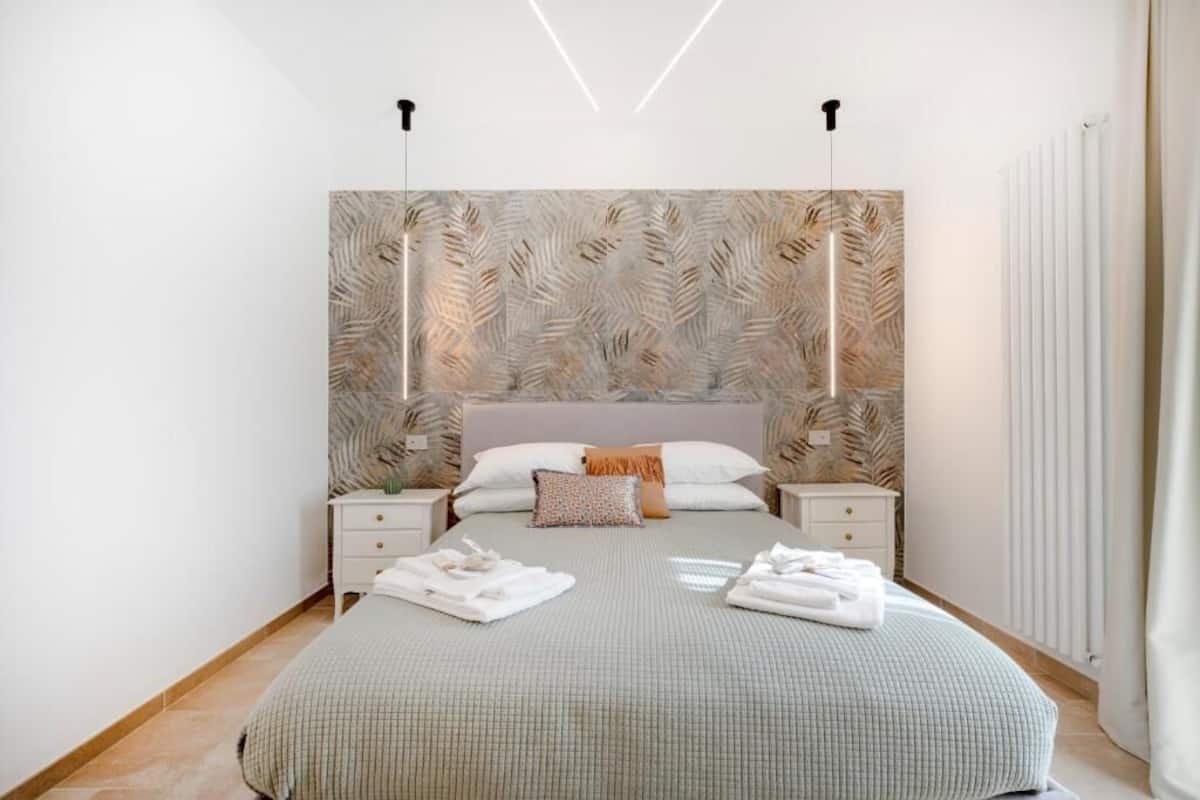 Un dormitorio con una cama grande, dos mesitas de noche, un cabecero con motivos de hojas y un radiador.