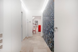 Um corredor com parede estampada, uma porta e uma área de jantar ao fundo.