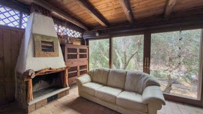 Ein gemütliches Zimmer mit Kamin, Holzmöbeln und großen Fenstern mit Blick auf Bäume.