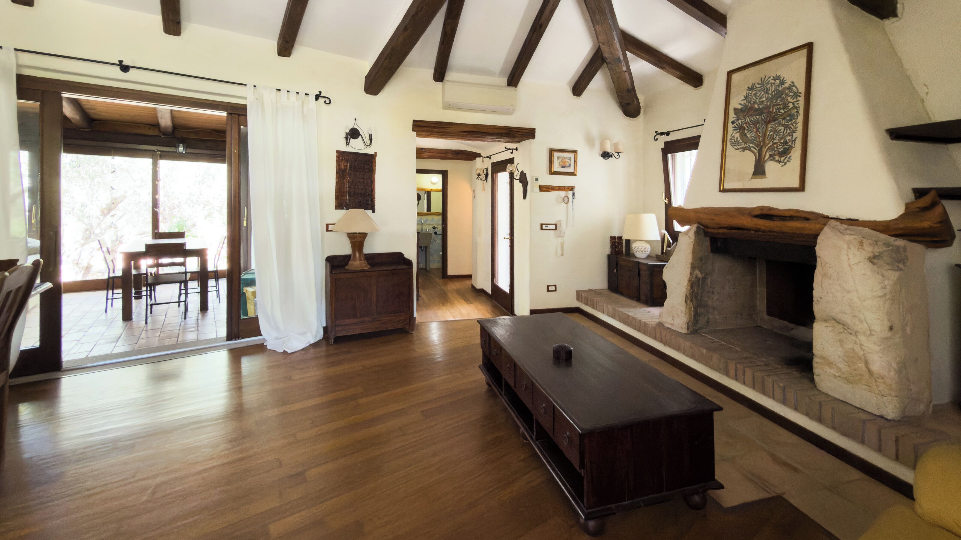 A spacious living room with wooden floors, a fireplace, a dining area with a table and chairs, and a hallway leading to another room.