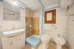 Une salle de bain avec une douche en pierre, un lavabo, des toilettes et un miroir.