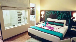 Hotellihuone, jossa on sänky, kylpyhuone suihkulla, yöpöytä ja seinään kiinnitetty valaisin.