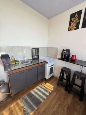 A compact kitchen with a sink, stove, and countertop appliances, a small stool, and a rug on the floor.