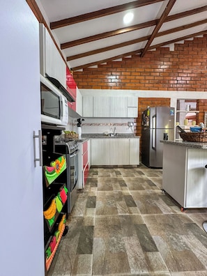 Una cocina con armarios blancos, pared de ladrillo, refrigerador de acero inoxidable y microondas.