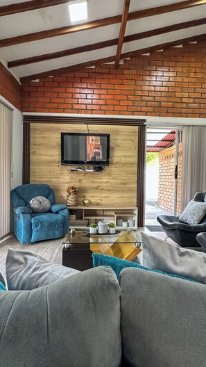 A living room with a brick wall, a mounted TV, a blue sofa, a grey sofa, and a glass coffee table.