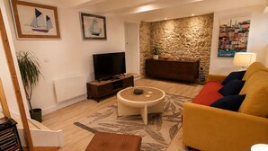 Ein Wohnzimmer mit einer Couch, einem Couchtisch, einem Fernseher, einer Steinwand und Kunstwerken an den Wänden.